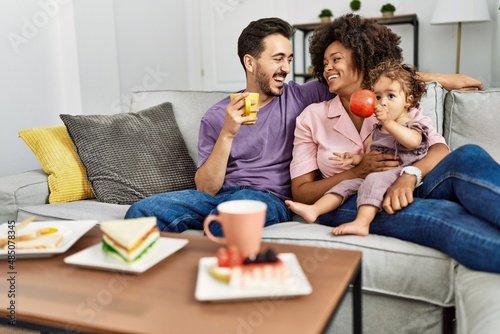 Couple and daughter having breakfast sitting on sofa at home