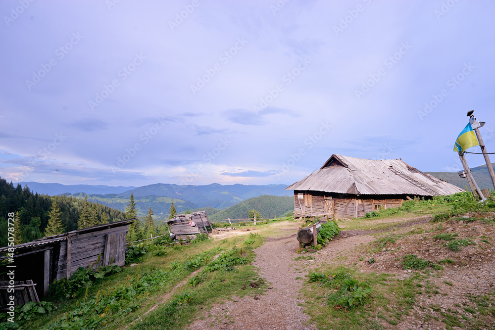 Beautiful mountains landscape with green meadow, sunset and wooden house. Carpathians, Ukraine.