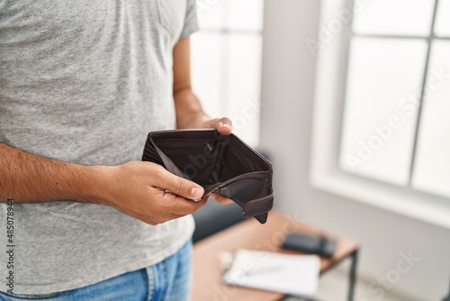 Young hispanic man showing empty wallet standing at home