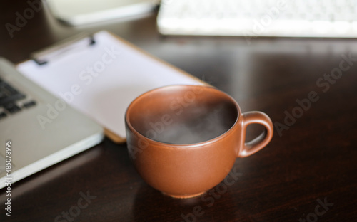 brown cup with hot drink and smoke, on work desk table