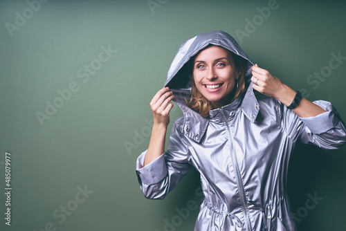 It's rain! Portrait of young woman wearing silver raincoat against green wall.