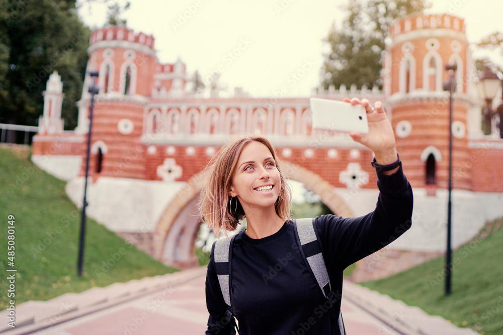 Travel and techology. Young woman taking photo on her smartphone on Tsaritsino Palace Park in Moscow, Russia.