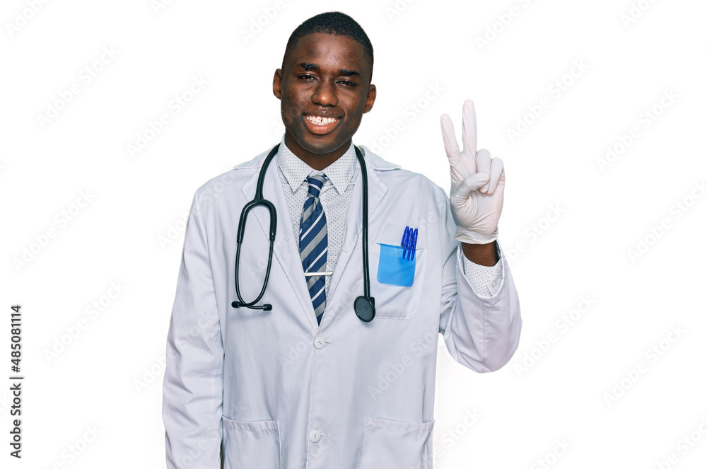 Young african american man wearing doctor uniform and stethoscope smiling with happy face winking at the camera doing victory sign. number two. Young african american man wearing doctor uniform and stethoscope smiling with happy face winking at the camera doing victory sign. number two.