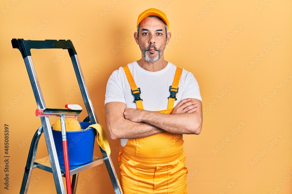 Handsome middle age man with grey hair window cleaner crossing arms making fish face with mouth and squinting eyes, crazy and comical. Handsome middle age man with grey hair window cleaner crossing arms making fish face with mouth and squinting eyes, crazy and comical.