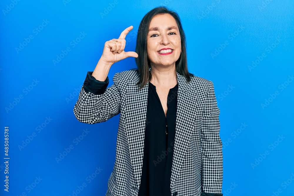 Middle age hispanic woman wearing business clothes smiling and confident gesturing with hand doing small size sign with fingers looking and the camera. measure concept. Middle age hispanic woman wearing business clothes smiling and confident gesturing with hand doing small size sign with fingers looking and the camera. measure concept.