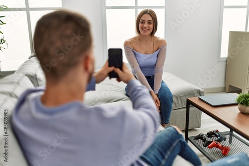 Young man making picture of his girlfriend using smartphone at home.