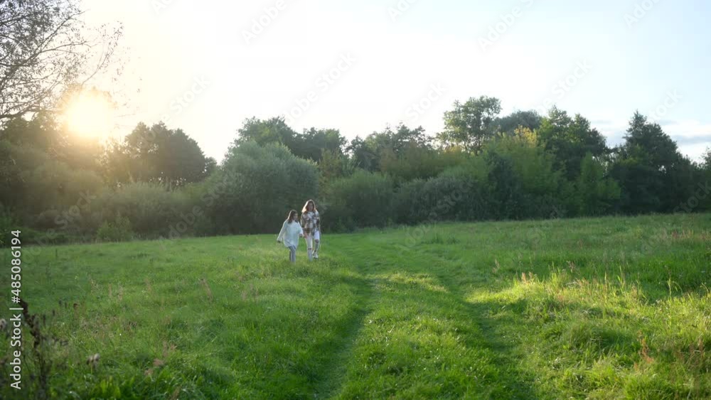 Happy young mum and daughter play together outdoor enjoy beautiful field of sunshine and spring grass while on a summer holiday. Family outdoor lifestyle. Happy young mum and daughter play together outdoor enjoy beautiful field of sunshine and spring grass while on a summer holiday. Family outdoor lifestyle.