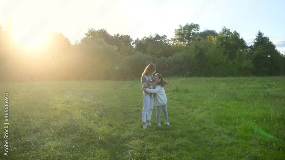 Happy young mum and daughter walking together outdoor enjoy beautiful field of sunshine and spring grass while on a summer holiday. Family outdoor lifestyle.