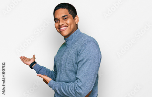 Young handsome hispanic man wearing casual sweatshirt inviting to enter smiling natural with open hand