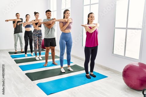 Group of young hispanic people smiling happy stretching at sport center.