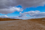 The dirt road goes into the distance under a bright blue sky with beautiful clouds.