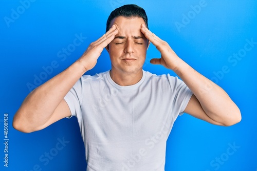 Handsome young man wearing casual white t shirt with hand on head, headache because stress. suffering migraine.