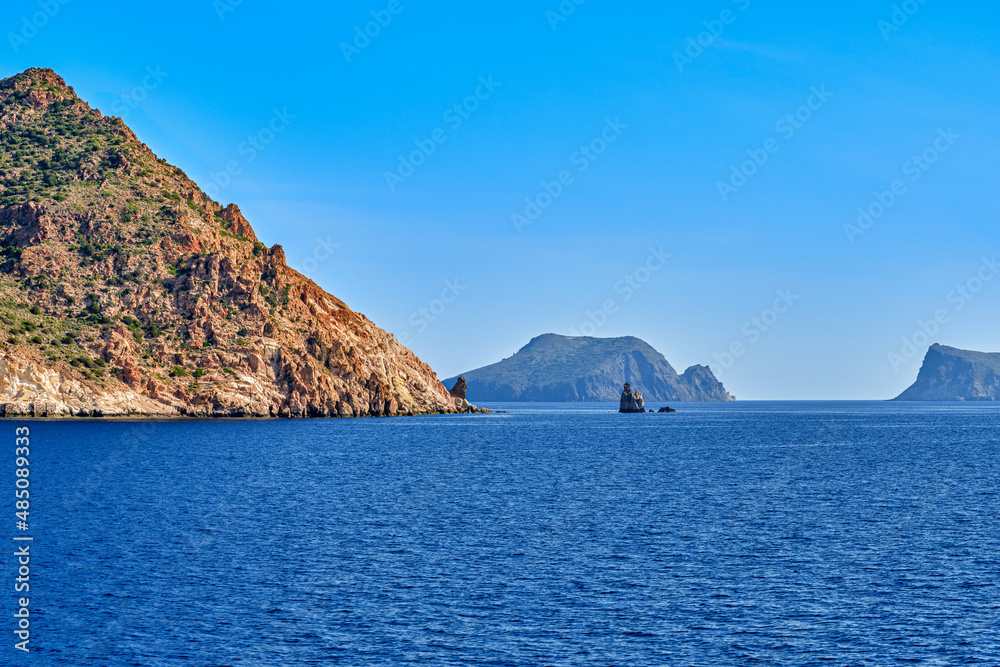Beautiful view of high hill slope of island in Mediterranean sea. Blue waters and sky, bright sunshine, summer day, rocks and isles in background. Beautiful view of high hill slope of island in Mediterranean sea. Blue waters and sky, bright sunshine, summer day, rocks and isles in background.