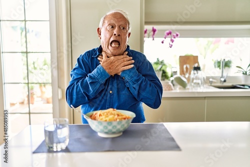 Senior man with grey hair eating pasta spaghetti at home shouting and suffocate because painful strangle. health problem. asphyxiate and suicide concept.