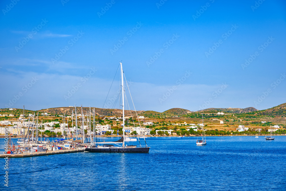 Beautiful summer day, sunshine in typical marina of Greek island. Sailboats and yachts at jetty. Whitewashed houses on hills. Mediterranean vacations.