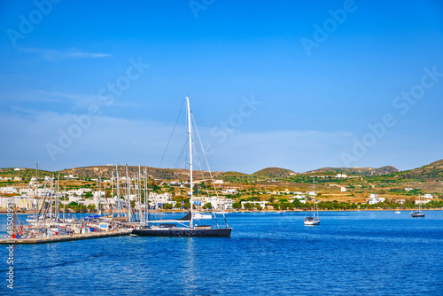 Beautiful summer day, sunshine in typical marina of Greek island. Sailboats and yachts at jetty. Whitewashed houses on hills. Mediterranean vacations.
