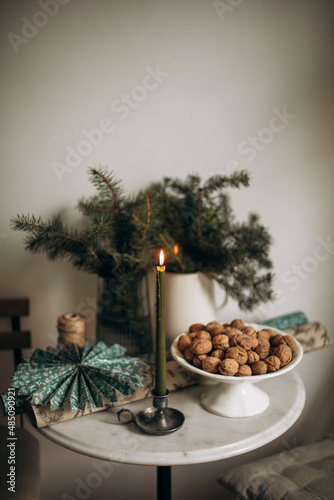burning tall candle in a vintage candlestick. green candle on white table with christmas decorations and walnuts in shell