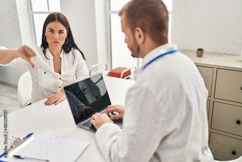 Young hispanic woman at the doctor with angry face, negative sign showing dislike with thumbs down, rejection concept
