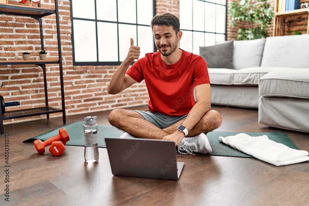 Fototapeta premium Young hispanic man watching training tutorial at home smiling happy and positive, thumb up doing excellent and approval sign