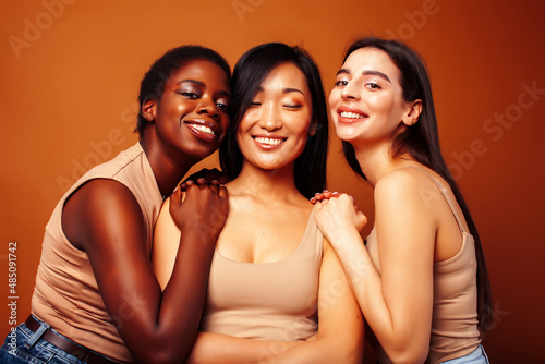 young pretty caucasian, african, scandinavian woman posing cheerful together on brown background, lifestyle diverse nationality people concept