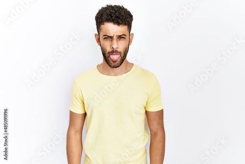 Arab young man standing over isolated background sticking tongue out happy with funny expression. emotion concept.