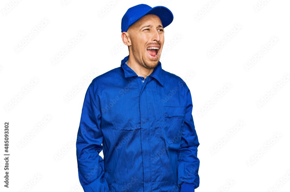Bald man with beard wearing builder jumpsuit uniform angry and mad screaming frustrated and furious, shouting with anger. rage and aggressive concept. Bald man with beard wearing builder jumpsuit uniform angry and mad screaming frustrated and furious, shouting with anger. rage and aggressive concept.