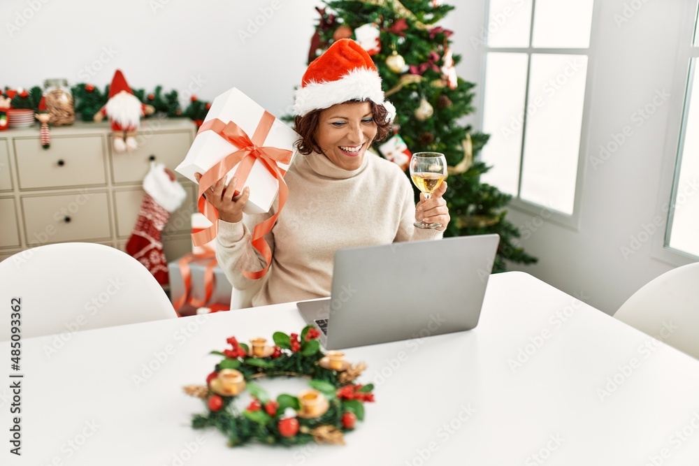 Middle age hispanic woman smiling happy wearing christmas hat having video call at home. Middle age hispanic woman smiling happy wearing christmas hat having video call at home.