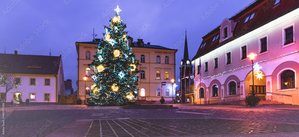 Fototapeta premium A deserted square photographed at night in the dark. The lights of Christmas decorations shine all around. There is a decorated Christmas tree in the square.
