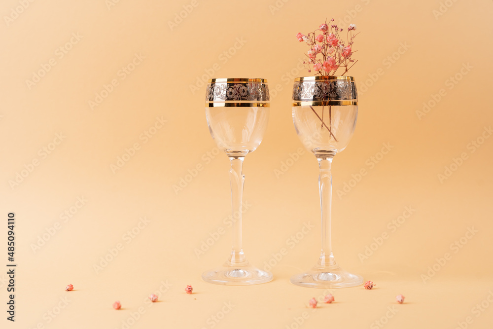 Two beautiful glass goblets on a high stem with golden edges and flowers inside on a nude cream fabric