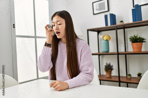 Young chinese girl using inhaler sitting on the table at home.