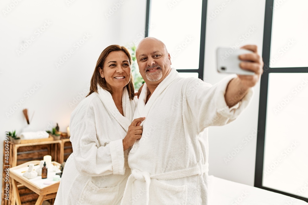 Obraz premium Middle age hispanic couple smiling happy making selfie by the smartphone at beauty center