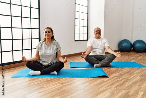 Middle age hispanic couple training yoga at sport center.