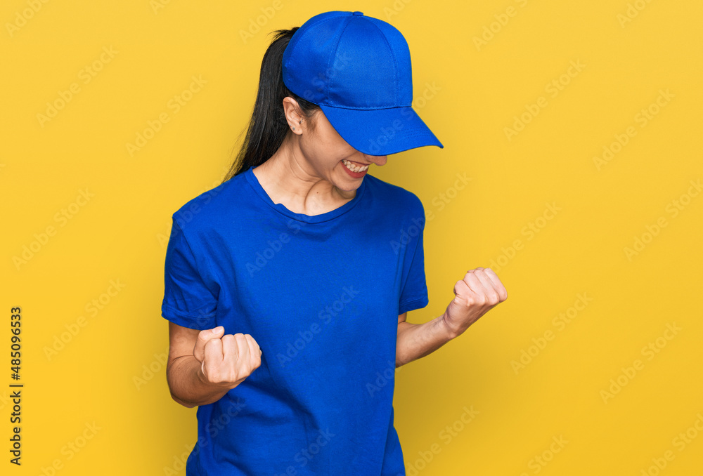 Young hispanic girl wearing delivery courier uniform very happy and excited doing winner gesture with arms raised, smiling and screaming for success. celebration concept.