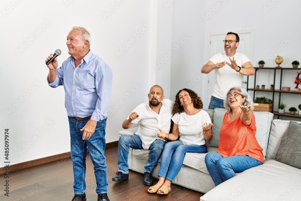 Group of middle age friends having party singing song using microphone at home.