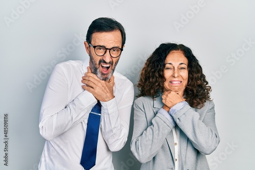 Middle age couple of hispanic woman and man wearing business office uniform shouting and suffocate because painful strangle. health problem. asphyxiate and suicide concept.