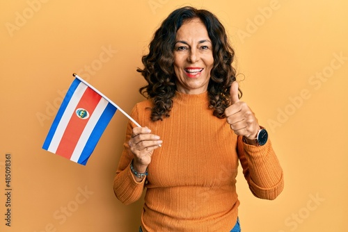 Middle age hispanic woman holding costa rica flag smiling happy and positive  thumb up doing excellent and approval sign