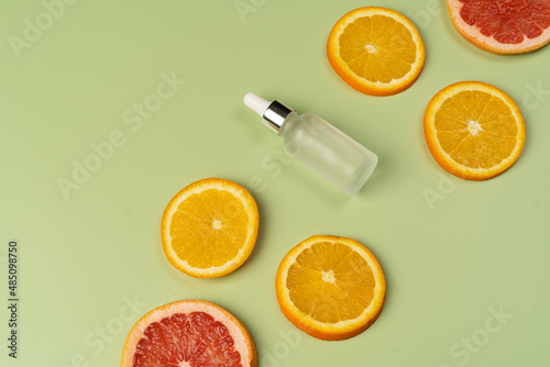 Natural vitamin C serum, skin care, essential oils. Cosmetic glass bottle with dropper and fresh juicy orange and grapefruit slices.
