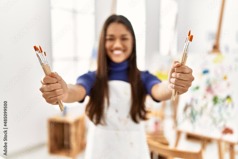 Young latin woman smiling confident holding paintbrushes at art studio Young latin woman smiling confident holding paintbrushes at art studio
