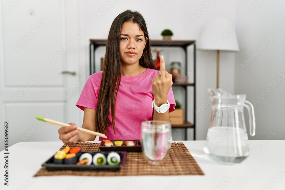 Young brunette woman eating sushi using chopsticks showing middle finger, impolite and rude fuck off expression Young brunette woman eating sushi using chopsticks showing middle finger, impolite and rude fuck off expression