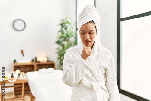 Young brunette woman wearing towel and bathrobe standing at beauty center feeling unwell and coughing as symptom for cold or bronchitis. health care concept.