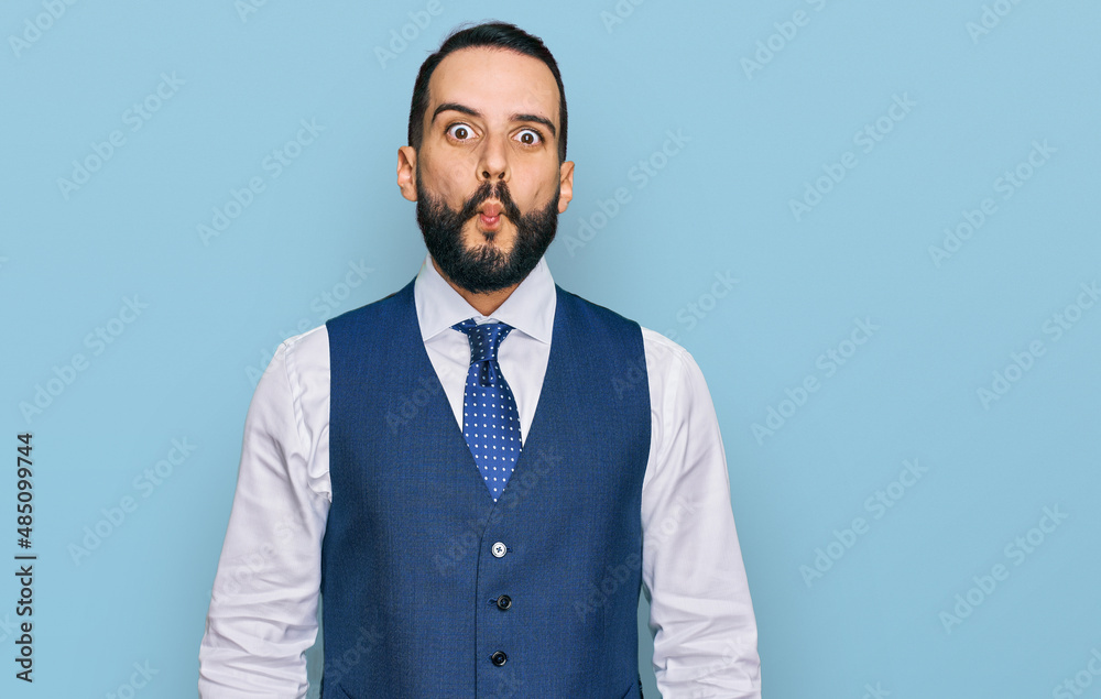Young man with beard wearing business vest making fish face with lips, crazy and comical gesture. funny expression.