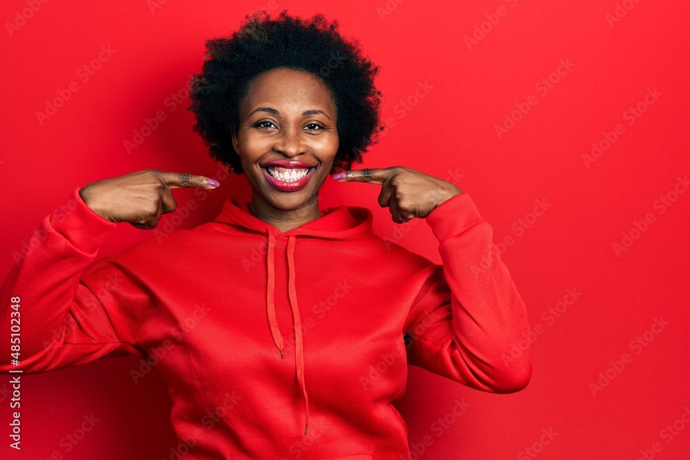 Young african american woman wearing casual sweatshirt smiling cheerful showing and pointing with fingers teeth and mouth. dental health concept. Young african american woman wearing casual sweatshirt smiling cheerful showing and pointing with fingers teeth and mouth. dental health concept.