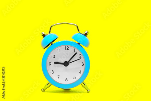 Blue classic retro alarm clock on yellow bright background with copy space