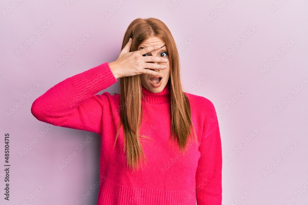 Young irish woman wearing casual clothes peeking in shock covering face and eyes with hand, looking through fingers afraid Young irish woman wearing casual clothes peeking in shock covering face and eyes with hand, looking through fingers afraid