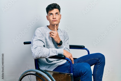 Young hispanic man sitting on wheelchair thinking concentrated about doubt with finger on chin and looking up wondering © Krakenimages.com