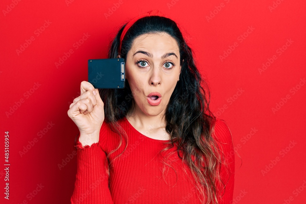 Young hispanic woman holding ssd memory scared and amazed with open mouth for surprise, disbelief face Young hispanic woman holding ssd memory scared and amazed with open mouth for surprise, disbelief face