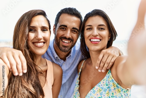 Three young hispanic friends smiling happy and hugging make selfie by the camera at the beach.