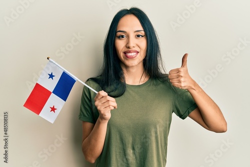 Young hispanic girl holding panama flag smiling happy and positive, thumb up doing excellent and approval sign