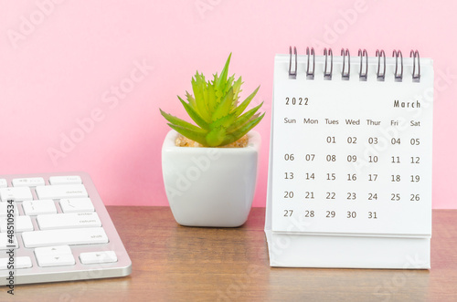 March 2022 desk calendar on wooden table with pink background.