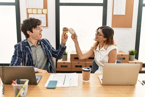 Two business workers smiling happy toasting with doughnuts at the office. photo